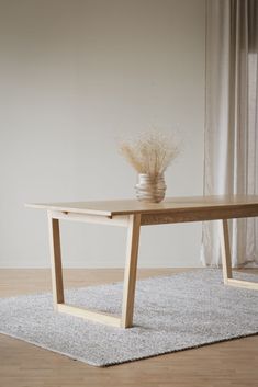 a wooden table sitting on top of a rug next to a vase with flowers in it