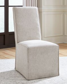 a beige upholstered chair in front of a window with white rug and wooden flooring