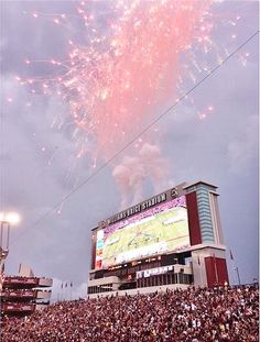 fireworks are lit up in the sky above a crowd at a football game on a cloudy day