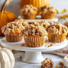 several muffins on a white cake plate with pumpkins in the back ground