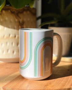 a coffee mug sitting on top of a wooden table next to a potted plant