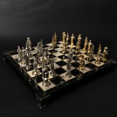 a chess board with gold and silver pieces on it's sides, sitting on a black surface