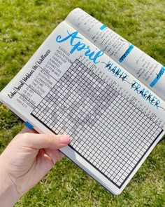 a person holding up a book with writing on it in front of some green grass