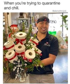 a man holding a bunch of toilet paper wrapped in red and white ribbon with greenery