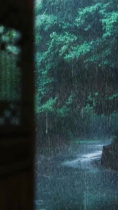 an open window with rain falling down on the ground and trees in the backround