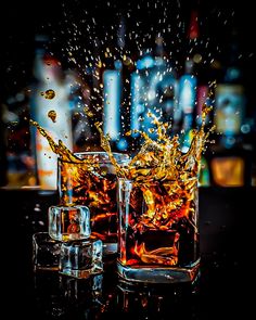 two glasses filled with liquid on top of a black table next to each other and splashing water