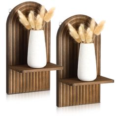 two white vases with feathers in them on wooden shelves against a white background for display