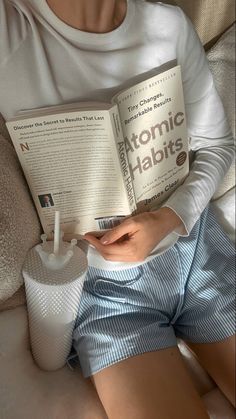 a person sitting on a couch reading a book and holding a drink in their hand