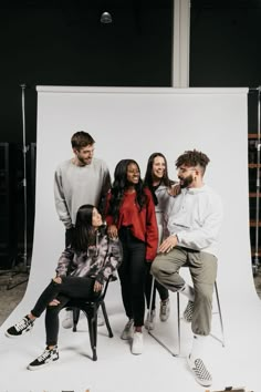 a group of people sitting around each other in front of a white backdrop with one person taking a photo