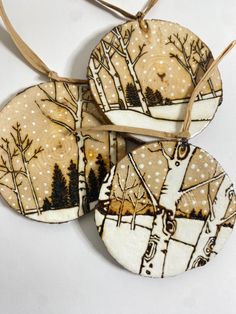 three ceramic ornaments with trees and snow on them are hanging from a string ornament