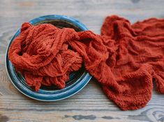 a blue plate topped with red cloth on top of a wooden table next to a bowl