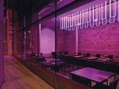 an empty restaurant with purple lighting in the windows and tables on the floor, along with brick walls