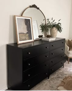 a black dresser with a mirror and potted plants on it in a living room