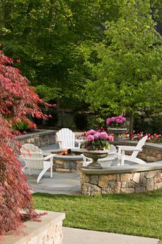 an outdoor patio with chairs and fire pit surrounded by flowers in the back yard area