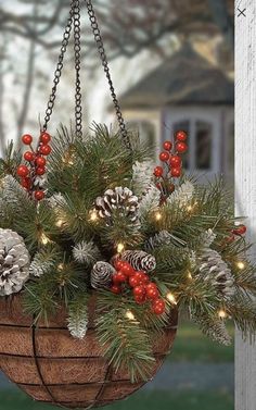 a hanging basket filled with pine cones and red berries is adorned with christmas lights, evergreens and other greenery