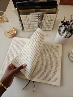 an open book sitting on top of a table next to a hand pointing at it