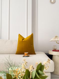 a white couch sitting next to a table with flowers on top of it and a yellow pillow