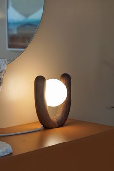 a wooden lamp sitting on top of a table next to a white wall and mirror