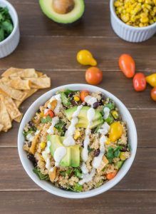 a bowl filled with rice, avocado, tomatoes and other vegetables next to tortilla chips