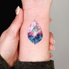 a woman's arm with a colorful diamond tattoo on her left wrist and the other hand behind her