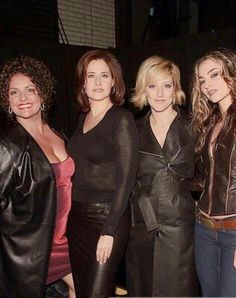 three women standing next to each other in front of a black wall and wearing leather jackets