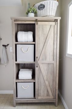 a bathroom cabinet with baskets and towels on it, next to a toilet paper roll