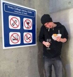 a man standing next to a sign holding a drink in his hand and eating food