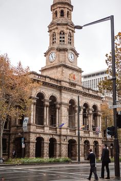 two men walking across the street in front of an old building with a clock tower