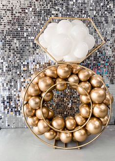 there is a gold ball sculpture in front of a mosaic wall with white balls on it