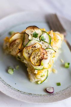 a slice of quiche with zucchini and onions on a plate next to a fork