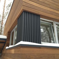 the side of a wooden house with snow on the ground and trees in the background