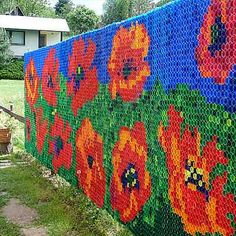 a colorful fence made out of plastic bottles with flowers painted on it in front of a house