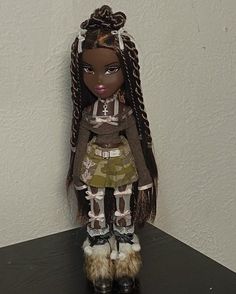 a doll with long hair and boots on top of a black table next to a white wall