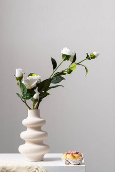 a white vase with flowers in it sitting on a table next to a cupcake