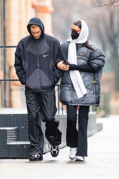 a man and woman walking down the street with their cell phones in hand, both wearing hoodies