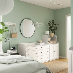 a bedroom with green walls and white bedding, mirror on the wall, plant in vase