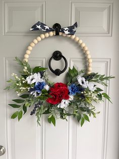 a wreath is hanging on the front door with red, white and blue flowers in it