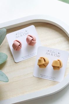 two pairs of pink and gold ear clips on a white tray next to a succulent plant