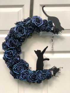 a black cat sitting on top of a blue wreath with roses in the shape of a crescent