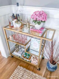 a gold bar cart with pink flowers and drinks on it in front of a white wall