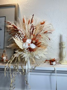 a vase filled with dried flowers on top of a mantle