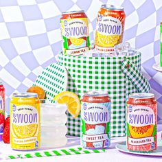 there are many cans of sodas and lemonade on the table with green checkered cloth