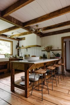 a large kitchen with wooden floors and white walls, has an island table surrounded by stools