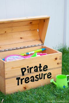 a wooden box filled with toys on top of grass next to a green watering can