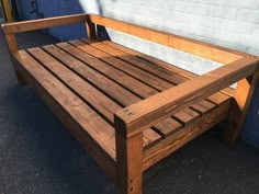 a wooden bench sitting in front of a white brick wall on a sidewalk next to a blue building