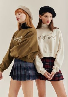 two young women standing next to each other wearing skirts and sweaters with words on them