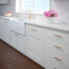 a kitchen with white cabinets and pink flowers in a vase on the sink countertop