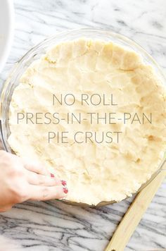 a pie crust in a glass dish with a hand reaching for it to be made