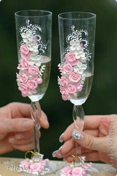 two people holding wine glasses decorated with pink roses and white pearls on the rims