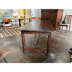 an old wooden table sitting on top of a cement floor next to chairs and tables